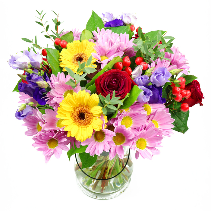 This image shows a lush, carefully composed bouquet brimming with colour and texture, arranged in a clear glass vase and photographed against a clean white background so no detail is lost. Deep red roses form the emotional core of the design, their velvety petals layered tightly in classic, romantic spirals. They are partnered with two radiant yellow gerbera daisies whose dark brown-orange centres and broad, open faces evoke sunshine breaking through a Stratford morning. Around these focal flowers, clusters of soft pink and lavender daisies or chrysanthemums create a halo of gentleness, each bloom offering fine, almost feathery petals around tiny yellow hearts, building a sense of volume and softness. Threaded among them, purple and lilac lisianthus provide a graceful contrast, their bell-shaped flowers and tender buds adding height, depth, and a cooler note that balances the warmer tones. Small bursts of bright red Hypericum berries nestle among the foliage, their rounded, glossy shapes supplying a playful, almost festive texture. A mix of rich green leaves - some broad and dark, others slender and lighter - frames the flowers, giving the impression of a bouquet freshly gathered and expertly styled at a Stratford flower shop after an early delivery from the market. The clear vase reveals cleanly cut stems resting in clear water, underscoring the freshness and professional care behind the design. The overall feeling is one of joyful celebration and thoughtful sentiment, perfectly suited to birthdays, congratulations, or simply sending a burst of colour to a home near Stratford station or the streets around The Grove.